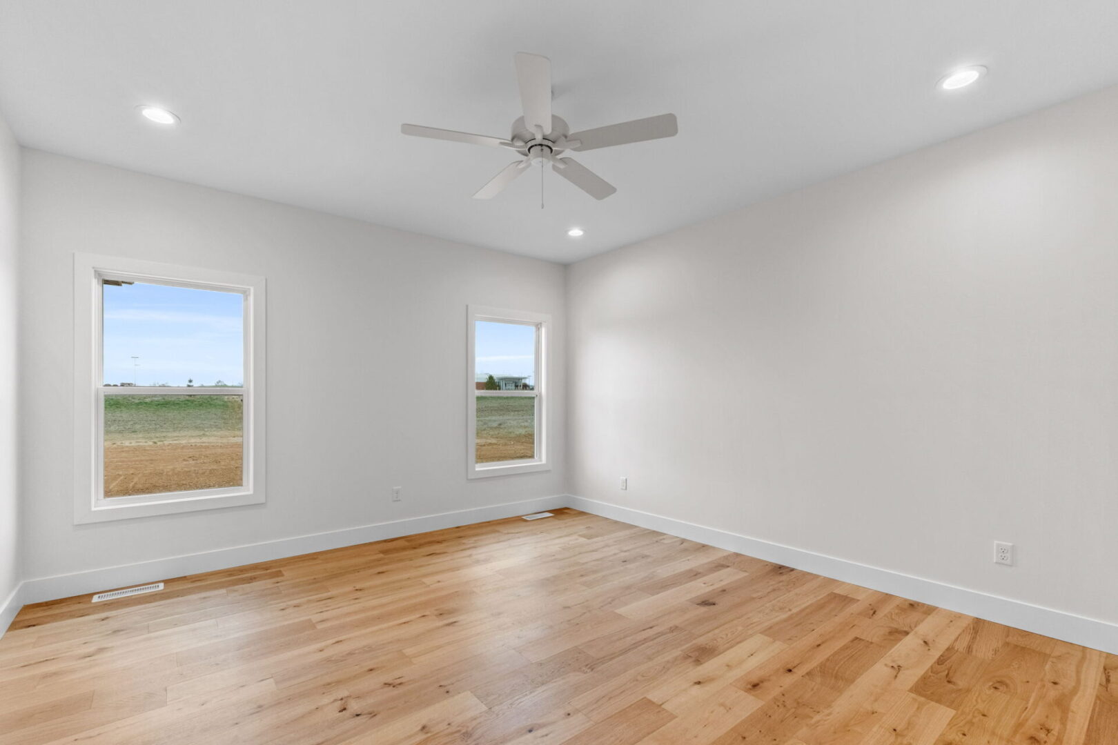 An empty room with a fan and two windows