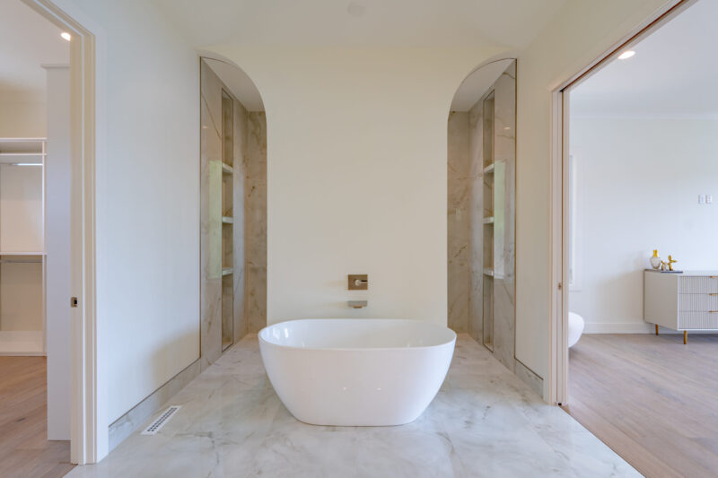 Primary suite bathroom with freestanding tub and arched entry to the large double head custom shower.