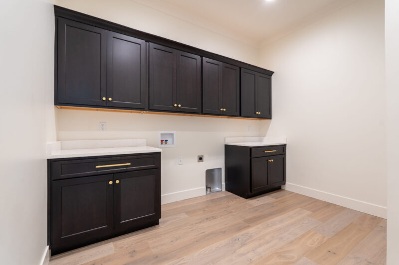 Main level laundry room with black cabinets and gold hardware.