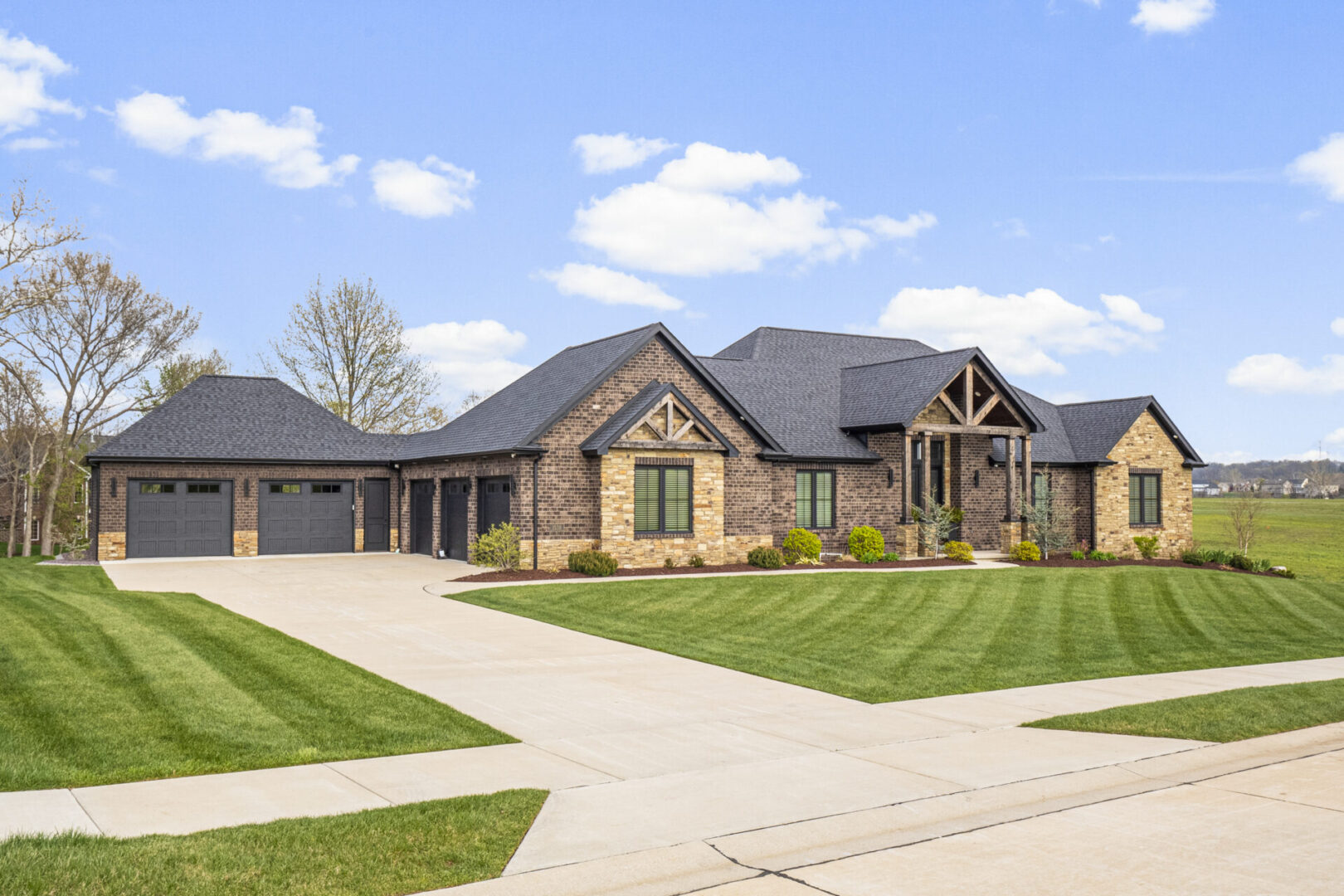 Drone A contemporary mountain-style home features a stone and brick exterior. Over the front entrance, dark wooden beams stretch out, adding a touch of grandeur.